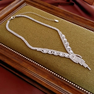Detail of silver V-shaped tassel necklace with sparkling zircons on green velvet