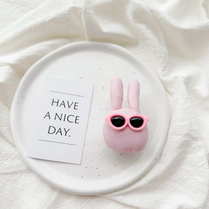 Detailed view of pink plush bunny phone grip with sunglasses on a white ceramic plate