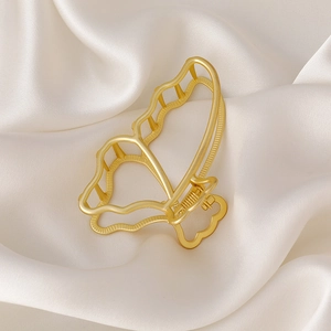 Detail van matgouden vlinder haarklem met een elegant opengewerkt golvend vleugelontwerp