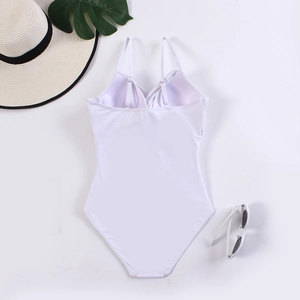 Flat lay of a white one-piece swimsuit with cross-back straps and summer accessories