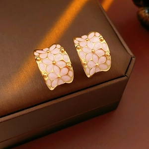 Détail de boucles d'oreilles fleurs en émail rose sur boîte en cuir et lumière chaude