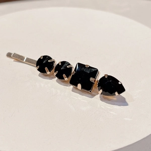 Detail of gold alloy hair clip with black faceted rhinestones on cream display plate