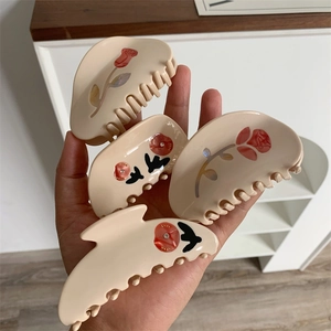 Detailed close-up of cream floral hair claws with red roses and sparkling rhinestones