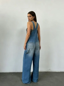 Détail de la salopette en jean bleu montrant le dos en Y et la coupe large sur modèle