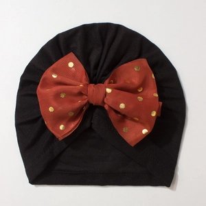 Detail of baby turban hat featuring a red bow with gold polka dots on soft black fabric