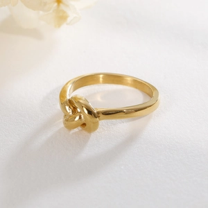 Close-up of a 18K gold-plated stainless steel knot ring on white textured surface