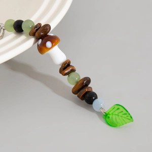 Dettaglio accessorio con fungo di vetro marrone, foglia verde e pietre occhio di tigre