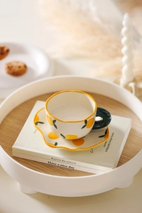 Close-up of ceramic coffee cup with hand-painted lemon pattern on wave-edged saucer
