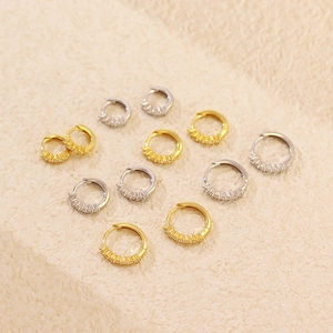Detailed view of silver and gold paved hoop earrings on textured beige fabric