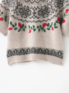 Close-up of beige knit sweater featuring red floral embroidery and geometric jacquard patterns
