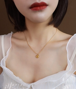 Detail of a minimalist 18k gold plated heart pendant necklace worn on a woman's collarbone