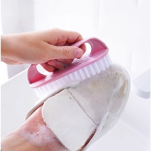 Pink plastic cleaning brush with white bristles scrubbing a dirty white canvas shoe