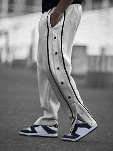 Detail of men's grey track pants featuring black side stripes and functional snap buttons