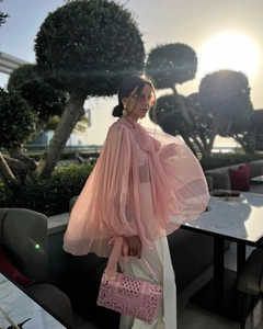 Detailed view of pink sheer organza top with lace handbag and white pants in garden