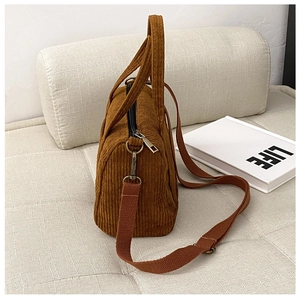 Detail of brown corduroy Boston bag with adjustable strap and metal buckle on soft sofa