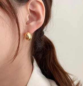 Close-up of a model wearing a shiny golden teardrop earring in a minimalist French style