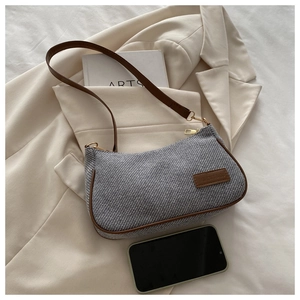 Detail view of grey textured underarm bag with brown leather trim and golden zipper