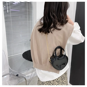 Back view of model wearing a black glossy heart-shaped crossbody bag with gold chain strap