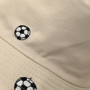 Nahaufnahme der Fußball-Stickerei und der Baumwolltextur auf einem beigen Fischerhut