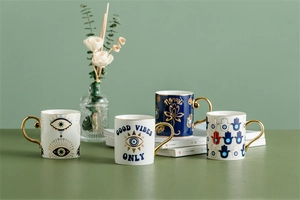 Detail of Nordic gold-rimmed Evil Eye ceramic mugs on a sage green background