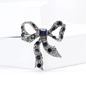Detailed close-up of a silver bow brooch with deep blue crystals on a white pedestal