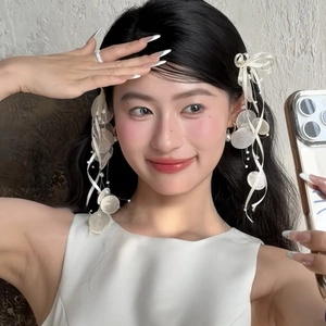 Close-up of white silk ribbon earrings with shell charms and pearl tassels on a model