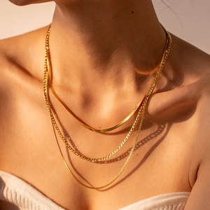 Three-layer gold snake and figaro chain necklace set worn by a model in warm light
