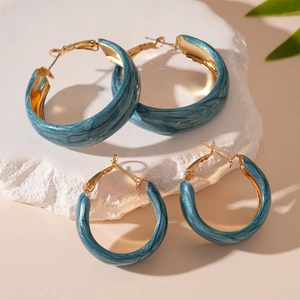 Retro teal marble resin C-shape hoop earrings with gold posts on stone pedestal