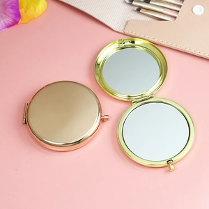 Dual-sided gold metal folding compact mirror shown open and closed on a pink surface