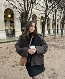 Detail shot of a dark brown shearling jacket with faux fur collar in a street style view