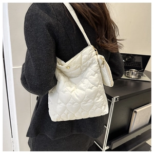 Detail view of heart-quilted cream tote bag with matching charm on a model
