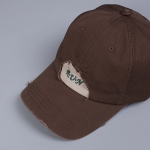 Close-up of distressed brim with R.U.N embroidery on a dark brown cotton baseball cap