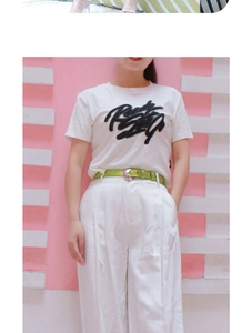 Detail of bright green belt paired with white wide-leg trousers and a graphic T-shirt