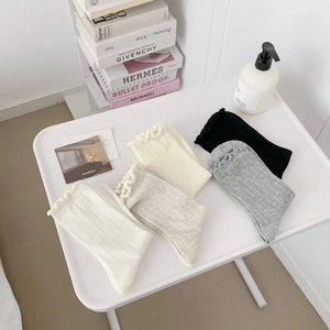 Detail of ruffle cuff cotton socks in Morandi tones with ribbed texture on white table