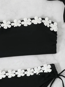 Detail of black bikini with white lace floral trim and elegant faux pearl embellishments
