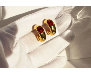 Detail of vintage gold C-shape earring with large oval red gemstone on white glove