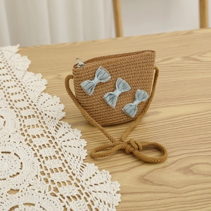 Detail of children's straw woven crossbody bag with blue lace bows on wood surface