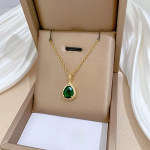 Detailed shot of emerald green pear-shaped necklace in a luxury champagne jewelry box