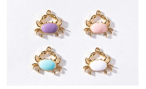 Detail of colorful crab pendants with gold frames in purple pink blue and white enamel