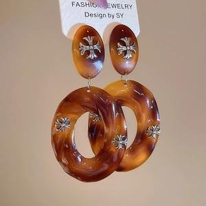 Detail view of amber resin hoop earrings with silver cross motifs on white tag