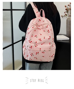 Detail of pink corduroy backpack with cherry print shown on model in a cozy indoor setting