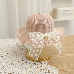 Vue détaillée d'un chapeau de paille rose avec un nœud en dentelle blanche à cœurs