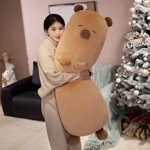Giant soft capybara long plush pillow toy being held in a cozy Christmas setting