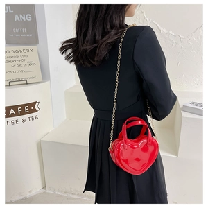 Red heart-shaped patent leather crossbody bag with gold chain strap on a model
