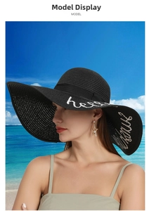 Detail of black straw sun hat with white hello sunshine embroidery and large brim