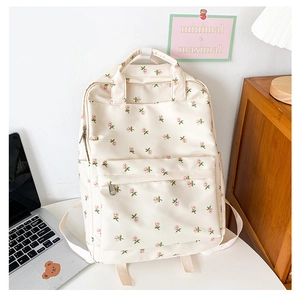 Detail of floral beige backpack showing rose prints and front pocket on a white desk