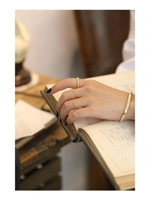 Close-up of golden quilted cuff bracelet and hammered rings worn on hand over book