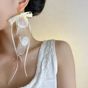 Close-up of long blue shell tassel earrings with elegant white ribbon bow on a model