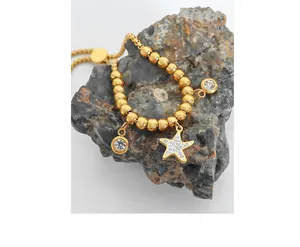 Detail of gold beaded bracelet with starfish pendant and crystal charms on rock