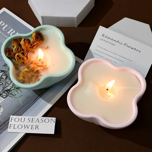 Close-up of petal shaped scented candle jars with burning wick and dried rose decoration